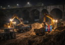 Excavators load sand into tractors during a nighttime sand mining operation near a river and railway bridge, illustrating illegal sand extraction activities in Mortad mandal.